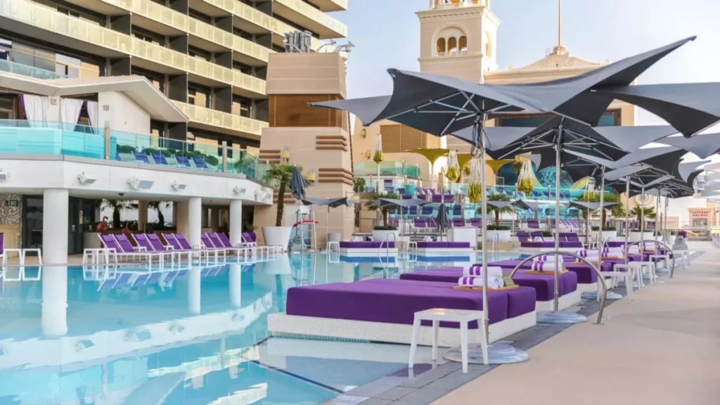 Purple daybeds and black umbrellas line the edge of the clear blue water at the Cosmopolitan Boulevard Pool.